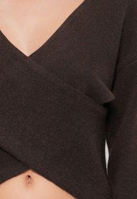 Haut enroulé marron avec des manches longues, décolleté en V et tissu en maille texturé, conçu pour se chevaucher à la taille.