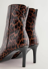 Leopard print ankle boots with a glossy finish, black stiletto heels, and textured material. Features a snug fit with a curved design.