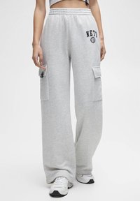 Hellgraue Cargo-Hosen mit weiter Beinform, ausgestattet mit zwei aufgesetzten Taschen und einem "NETS"-Logo. Hergestellt aus weichem, strukturiertem Stoff.
