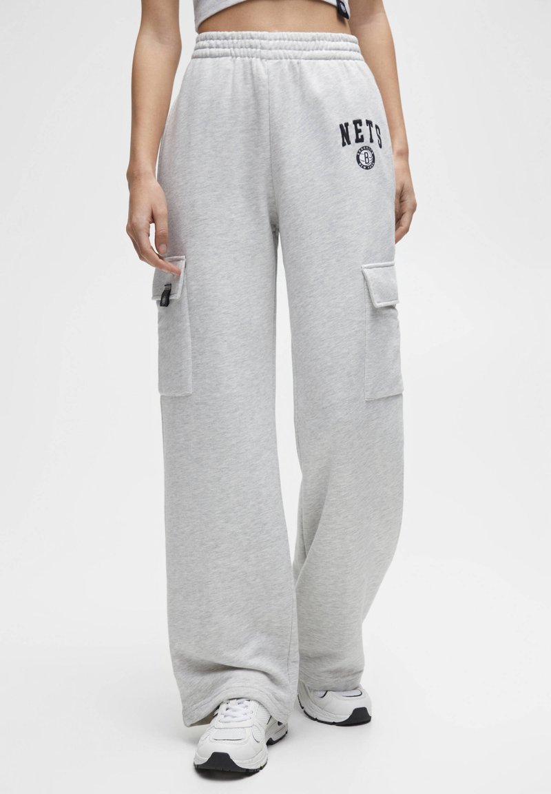 Hellgraue Cargo-Hosen mit weiter Beinform, ausgestattet mit zwei aufgesetzten Taschen und einem "NETS"-Logo. Hergestellt aus weichem, strukturiertem Stoff.