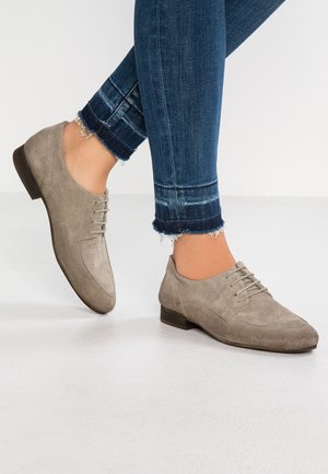 Chaussures à lacets en daim gris avec un petit talon, présentant une finition lisse et un design classique. Portées avec un jean bleu usé.