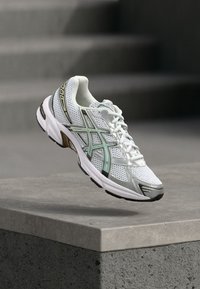 Balti bėgimo batai su tinkleliu, šviesiai žali ir juodi akcentai, paminkštintas kaklas ir tekstūruotas padas sukibimui, demonstruojantis suoformuotą dizainą.
