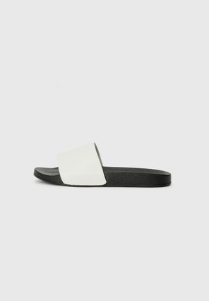 Sandale en caoutchouc blanc à glissière avec une large sangle et une semelle noire texturée, présentant une surface lisse et un design minimaliste.