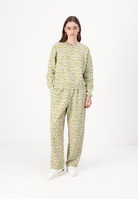 Conjunto de roupa de lazer cinza claro com padrão de bananas, feito em tecido suave. A parte de cima tem um corte descontraído; as calças são largas com um cós elástico.