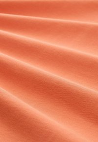 Textil i mjuk korallfärg, med en slät yta och synliga veck samt ett subtilt vävt mönster.