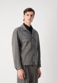 Grau karierte Jacke mit Stehkragen, Frontknopfverschluss und zwei Brusttaschen; strukturierter Stoff, lockere Passform und lange Ärmel.