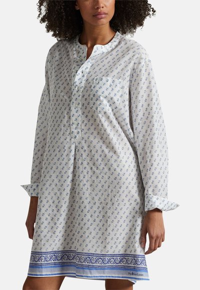 Femme portant une chemise de nuit blanche à manches longues avec un petit imprimé floral bleu et une bordure décorative bleue à l'ourlet, une poche avant et une patte de boutonnage partielle.