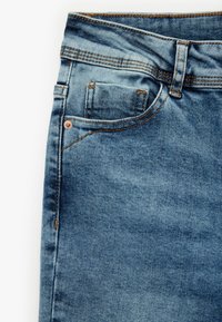 Jeans de mezclilla azul claro con una textura desgastada, que cuentan con costuras naranjas, un bolsillo frontal para monedas y un diseño clásico de cinco bolsillos.
