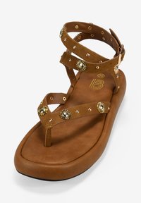 Infradito in suede marrone con multiple cinghie incrociate, decorazioni a forma di raggi di sole in oro e suola imbottita.