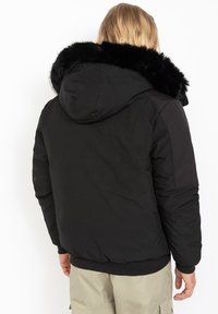 Schwarze gepolsterte Jacke mit einer großen Kapuze aus Kunstpelz, glatte Oberfläche, elastische Bündchen und Saum, mit einem minimalistischen Design ohne sichtbare Logos.