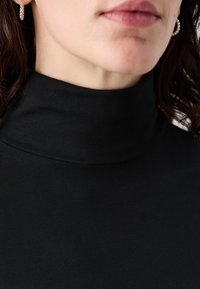 Svart höghalsad topp i slitstark tyg. Har en elastisk, figurnära design med rena sömmar och en subtil lyster.