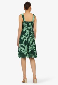 Grünes Blumenkleid mit eng anliegendem Oberteil und ausgestellt Rock. Verfügt über breite Träger, gesmokten Rücken und ein plissiertes Design mit Blattform.