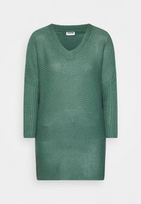 Grön stickad tröja med V-ringning, trekvartslånga ärmar och löst sittande passform. Texturen är öppen väv, vilket ger ett lätt utseende.