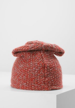 Bonnet en laine tricoté rouge et gris avec un sommet plié, reposant sur une surface blanche sur fond gris clair uni.