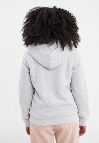 Sudadera gris con capucha ajustable y puños acanalados. Combinada con pantalones rosa claro, que muestran una tela suave y un ajuste cómodo.