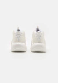Baskets blanches avec un design en cuir lisse et en maille, forme arrondie, col rembourré et lanière au talon pour un enfilage et un retrait faciles.