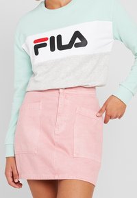 Sudadera azul claro y gris con el logo de "FILA" en negro y rojo; combinada con una falda de mezclilla rosa con dos bolsillos delanteros.