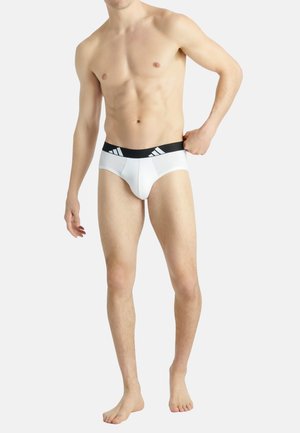Weiße Baumwollunterhosen mit einem schwarzen Bund, der drei weiße Streifen aufweist. Das Design ist enganliegend, hat eine glatte Textur und einen niedrigen Schnitt.