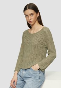 Gebreide trui in olijfgroen, met een gestructureerd patroon en lange mouwen, gecombineerd met high-waisted blauwe denim jeans.
