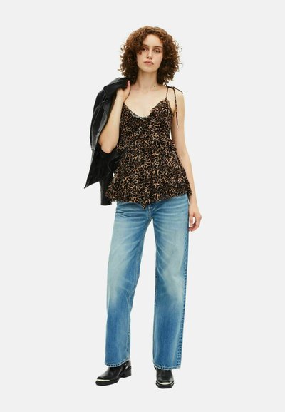 Top peplum noir et beige à motif avec de fines bretelles et un ourlet froncé, associé à un jean large bleu clair et des bottines noires.