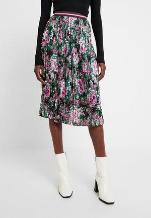 Woman wearing a pleated floral midi skirt in pink and green with a striped waistband, black long-sleeve top, and white heeled ankle boots.