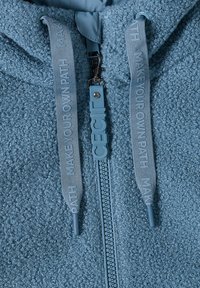 Haut en polaire bleu avec une surface texturée, doté d'une fermeture éclair, d'un tirette en caoutchouc et de cordons de serrage avec du texte en relief.