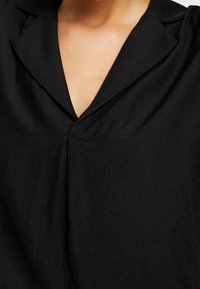 Chemise en lin noir avec col à revers et décolleté en V profond, dotée d'une texture subtile et d'une coupe ample. Design simple et polyvalent.