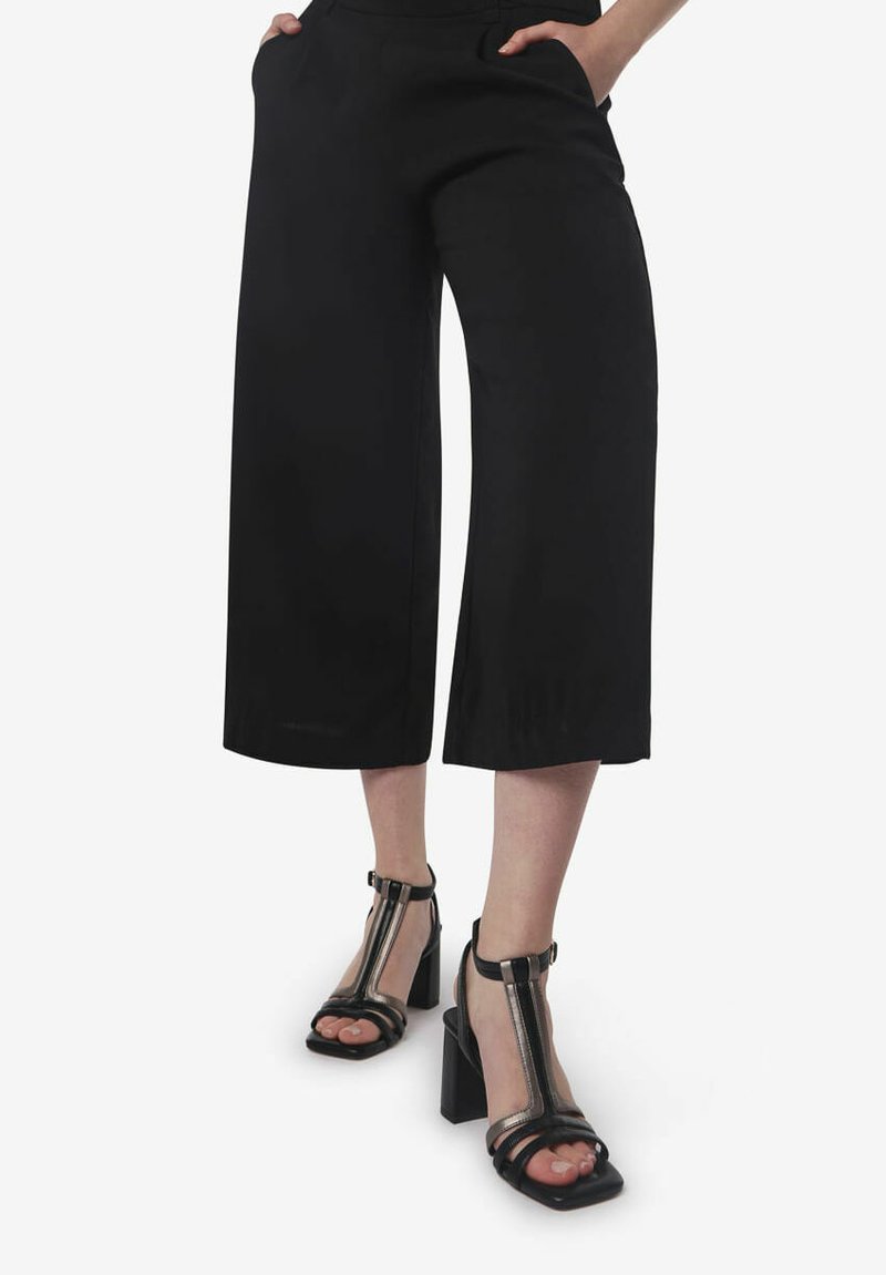 Zwarte wijdvallende culotte-broeken met zijzakken. Gepaard met zwarte sandalen met hielbandjes, voorzien van een transparante accent en een chunky hak.