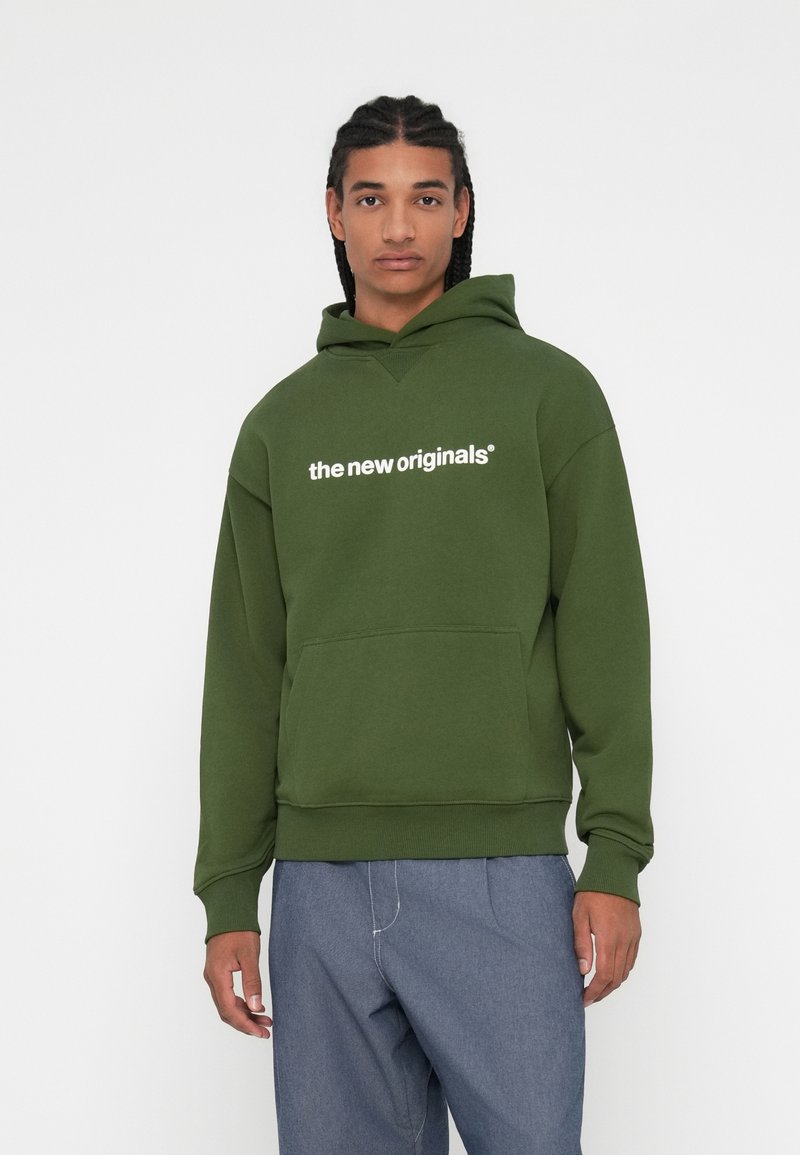 Zelena kapuca iz mehkega materiala, z žepom za kenguru, rebrastimi manšetami in belim napisom "novi originiali" čez prsni del.