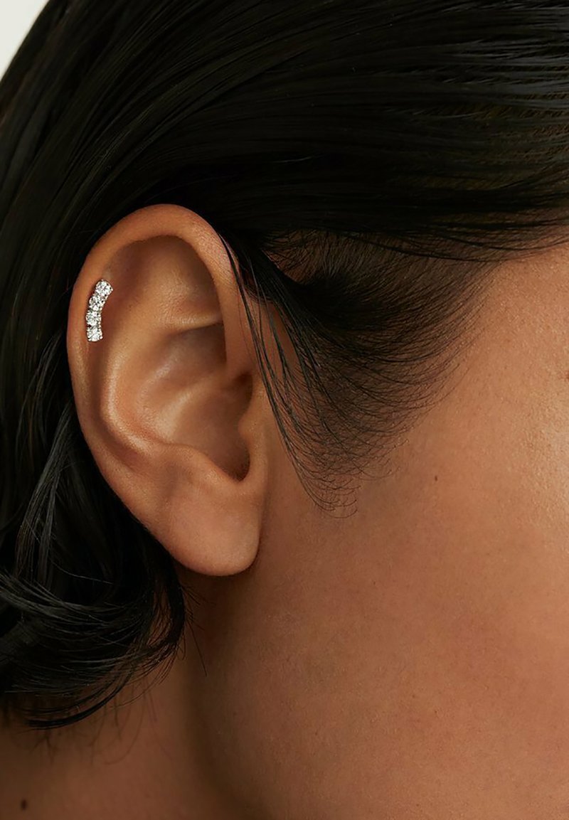 Orecchino cuff in argento con un design curvo, adornato con piccole gemme trasparenti, posizionato su un orecchio umano con capelli scuri.