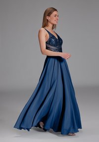 Pitkä, valuvan tuntuinen iltapuku sinisestä satiinista. Helmillä koristeltu paita, jossa V-pääntie ja säädettävät olkaimet. Lattiapituinen hame luo dramaattisen siluetin.