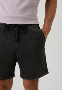 Black denim shorts with an elastic waistband and drawstring, featuring side pockets and a small logo detail on the left leg.