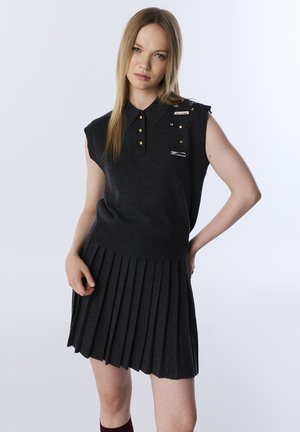 Polo sans manches gris charbon avec patte de boutonnage à trois boutons et épingles décoratives, associé à une jupe plissée en même matériau.