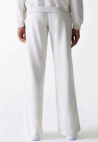 Hellgraue Sweatpants mit lockerer Passform, die eine weiche Textur und seitliche Streifenverzierungen aufweisen. Der Stoff ist glatt und leicht elastisch.