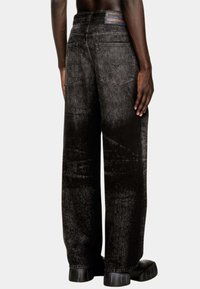 Jeans in denim neri a gamba larga con una texture sbiadita, dotati di due tasche posteriori e un'etichetta con il marchio sulla vita. Design minimalista.