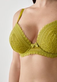 Limonkowy koronkowy biustonosz z falbaniastym brzegiem, kwiatowym wzorem, wsparciem w postaci fiszbin oraz małym kokardkowym detalem na środku. Regulowane ramiączka.