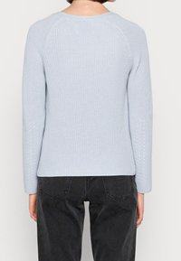 Ljusblå stickad tröja med rund halsringning, långa raglanärmar och ett strukturerat mönster vid muddarna och fållen. Stylerad med svarta byxor.