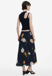 Sort ærmeløs top parret med en svævende, mørk blomsterkjole med gule og hvide tusindfryd. Silhuetten er afslappet og ankel-længde.