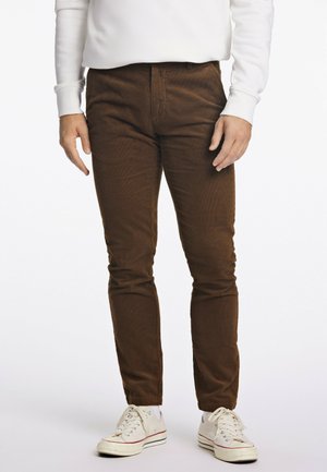 Pantaloni di velluto a coste marroni con una vestibilità slim, dotati di tasche anteriori e una texture liscia; abbinati a sneakers bianche per un contrasto.