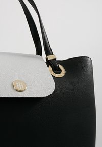 Sac à main en cuir noir avec un rabat texturé argenté, des accents en or et un détail de logo. Doté de deux poignées noires pour le transport.