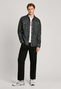 Donkerdenim shirt met een knoopsluiting, twee borstzakken, gecombineerd met zwarte broek en witte sneakers met grijze accenten.