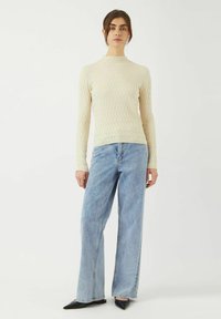 Vit ribbad långärmad topp med hög krage, kombinerad med ljusblå vida jeans och svarta spetsiga ballerinas. Enkelt, rent design.