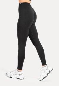 Schwarze Leggings mit hoher Taille und strukturiertem Muster, gefertigt aus einem glatten, elastischen Stoff, der sich dem Körper anpasst und vollständige Bedeckung bietet.