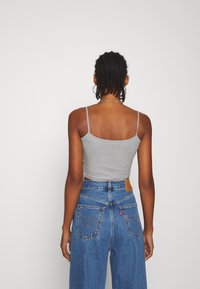 Débardeur gris ajusté avec fines bretelles, associé à un jean denim bleu taille haute avec une étiquette de marque et des poches arrière visibles.