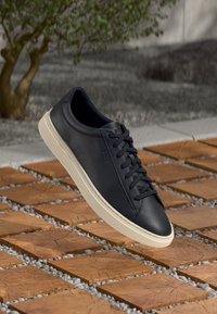 Zapatilla de cuero azul marino con parte superior texturizada, punta redonda y suela de goma blanca. Presenta un diseño sencillo de cordones y detalles mínimos.