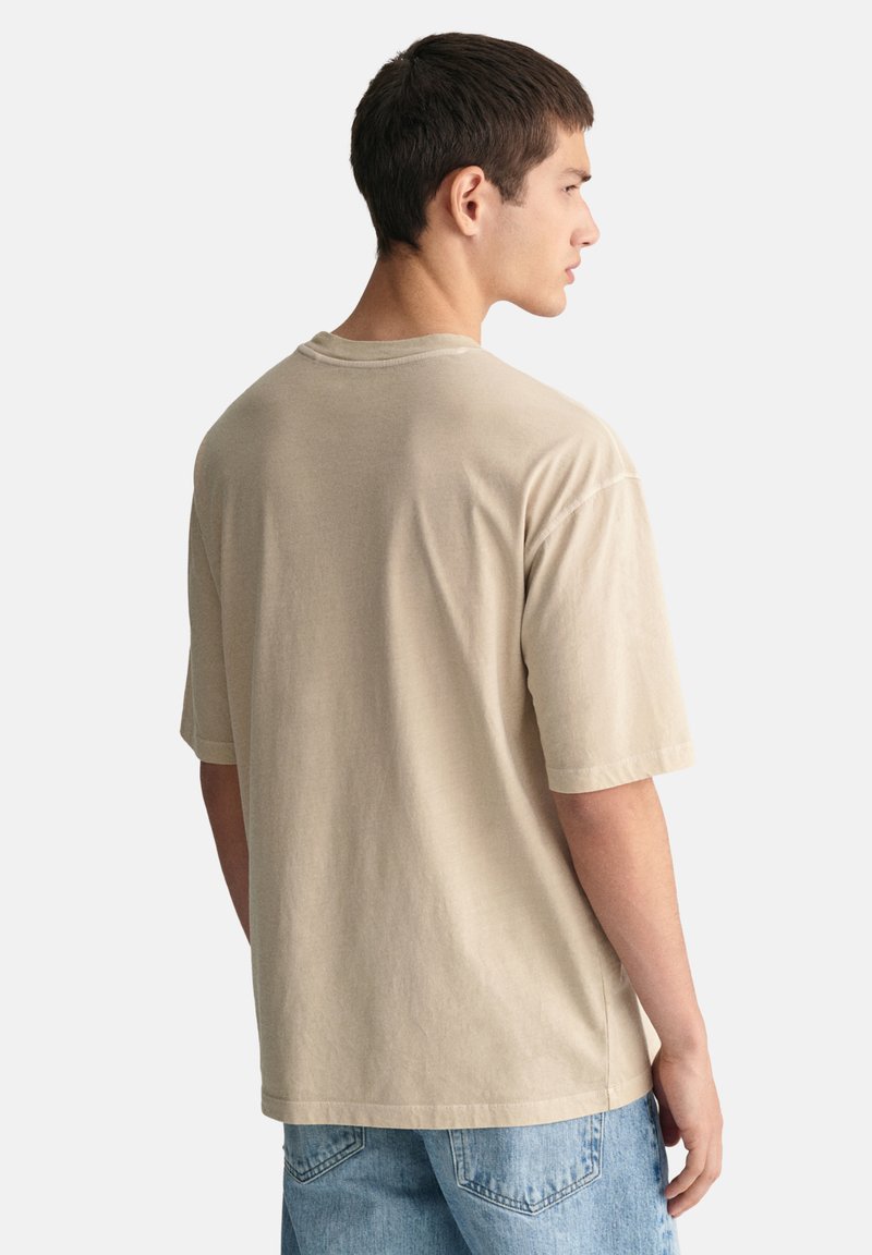 Camiseta de algodón beige, de manga corta, corte relajado, escote redondo, diseño liso, sin patrones ni acentos visibles, combinada con jeans de color azul claro.