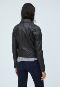 Czarna skórzana kurtka z pikowanym wzorem na ramionach, slim fit, wysoki kołnierz i zapięcia na zamek, noszona na szarym t-shircie i niebieskich dżinsach.