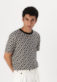 Zwart-witte korte mouwen t-shirt met geometrisch patroon en contrasterende zwarte halslijn, gecombineerd met lichtgekleurde broek.
