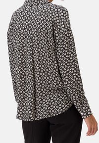 Blusa nera a maniche lunghe con un motivo geometrico bianco, colletto alla francese e vestibilità comoda, realizzata in tessuto leggero.