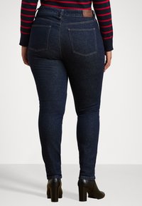 Mørkeblå skinny-jeans med detaljer på baklommene, solid midjebånd og en jevn tekstur, parret med svarte høyhælede ankelstøvletter.